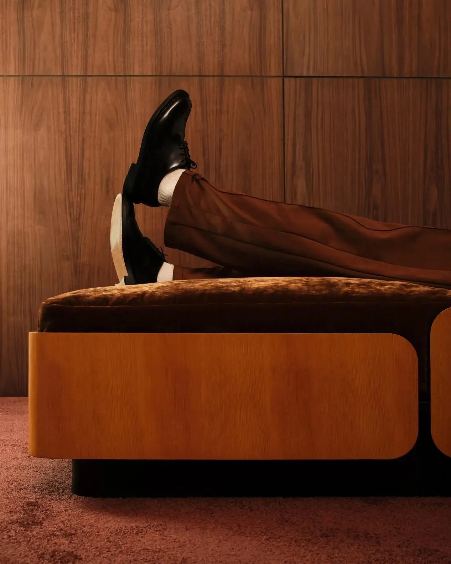 Black lace-up shoes resting on a velvet ottoman against wood paneling