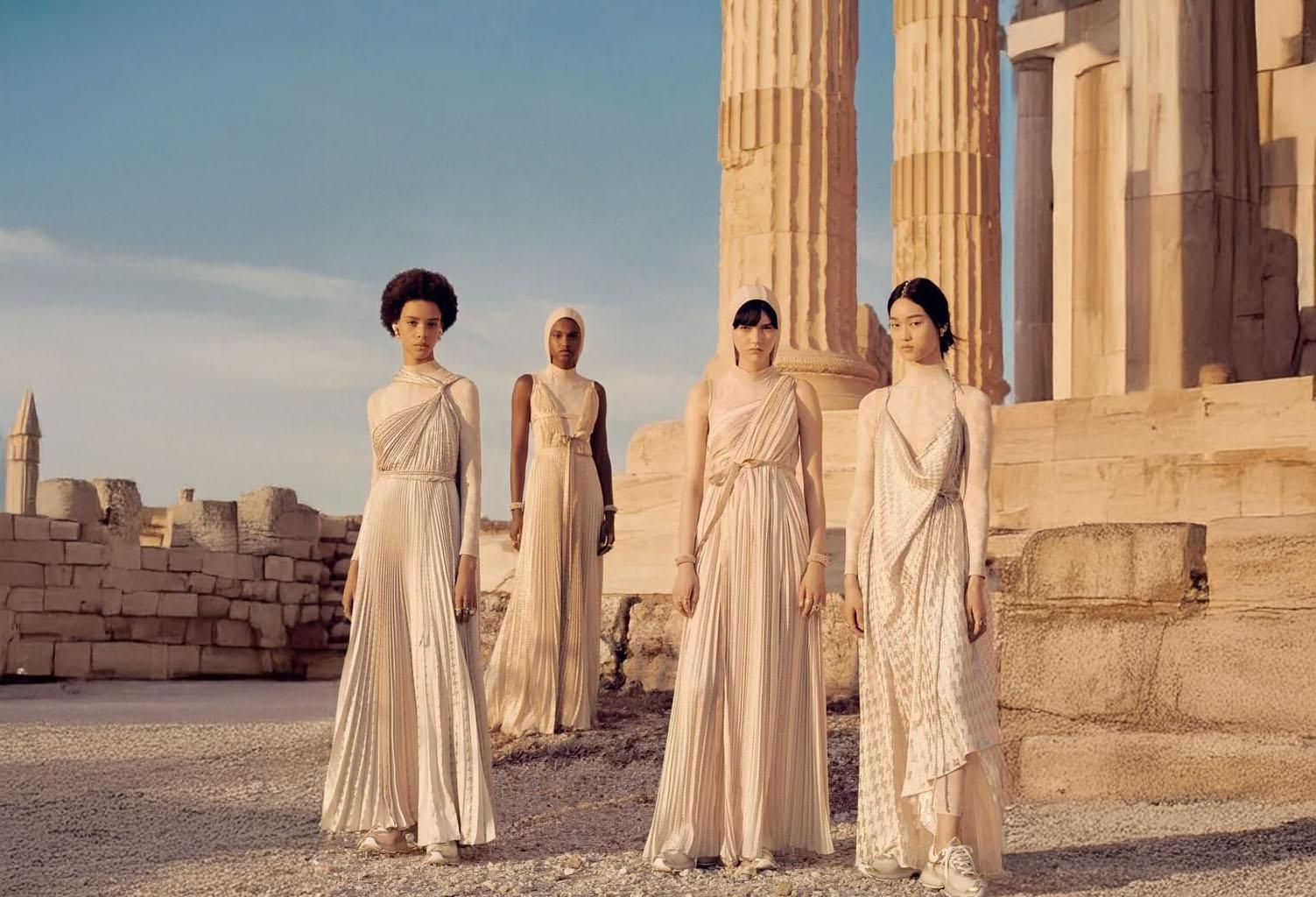Four models in pleated ivory gowns standing before ancient stone columns at dusk